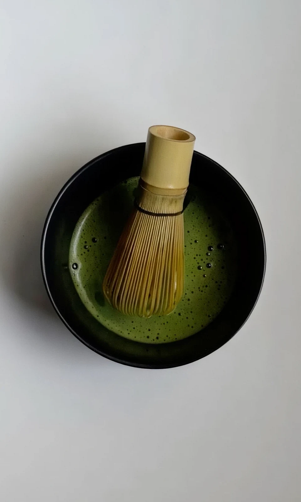 Overhead of a black tea bowl with a bamboo whisk resting in whisked matcha