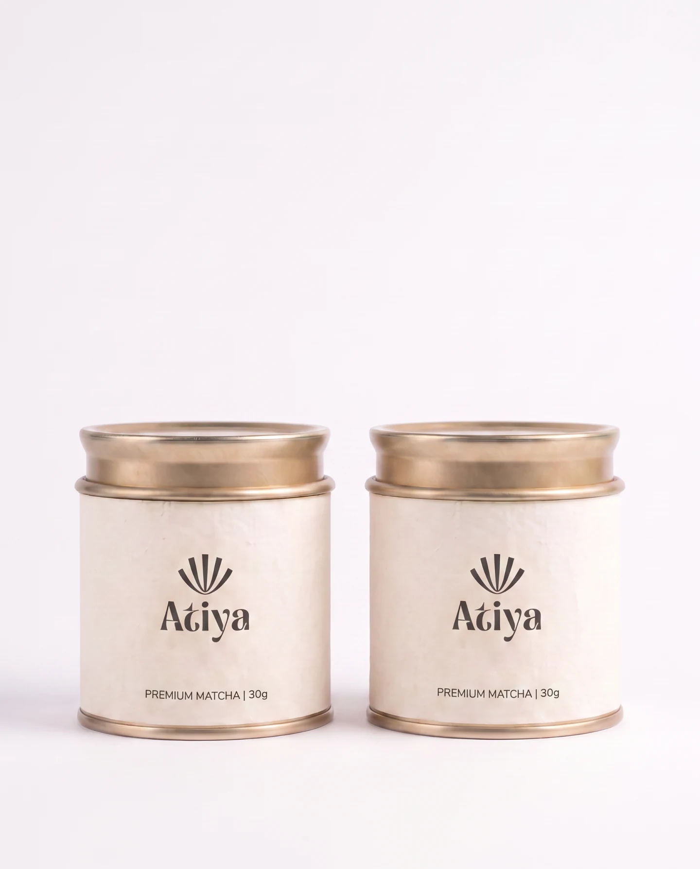 Two Atiya matcha tins side by side on a plain white ground, lids on, showing the front label