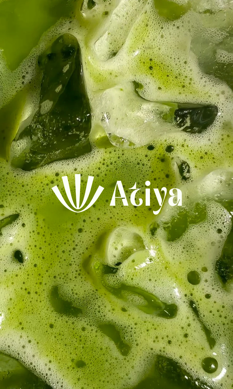 The Atiya symbol and wordmark in white over the frothed surface of an iced matcha