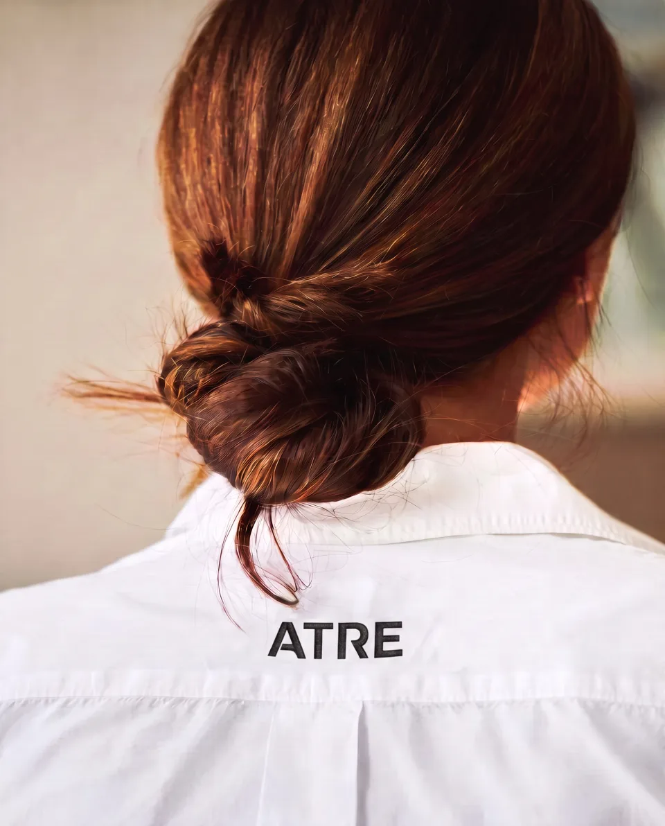 The back of a white service shirt printed ATRE, a low bun above it