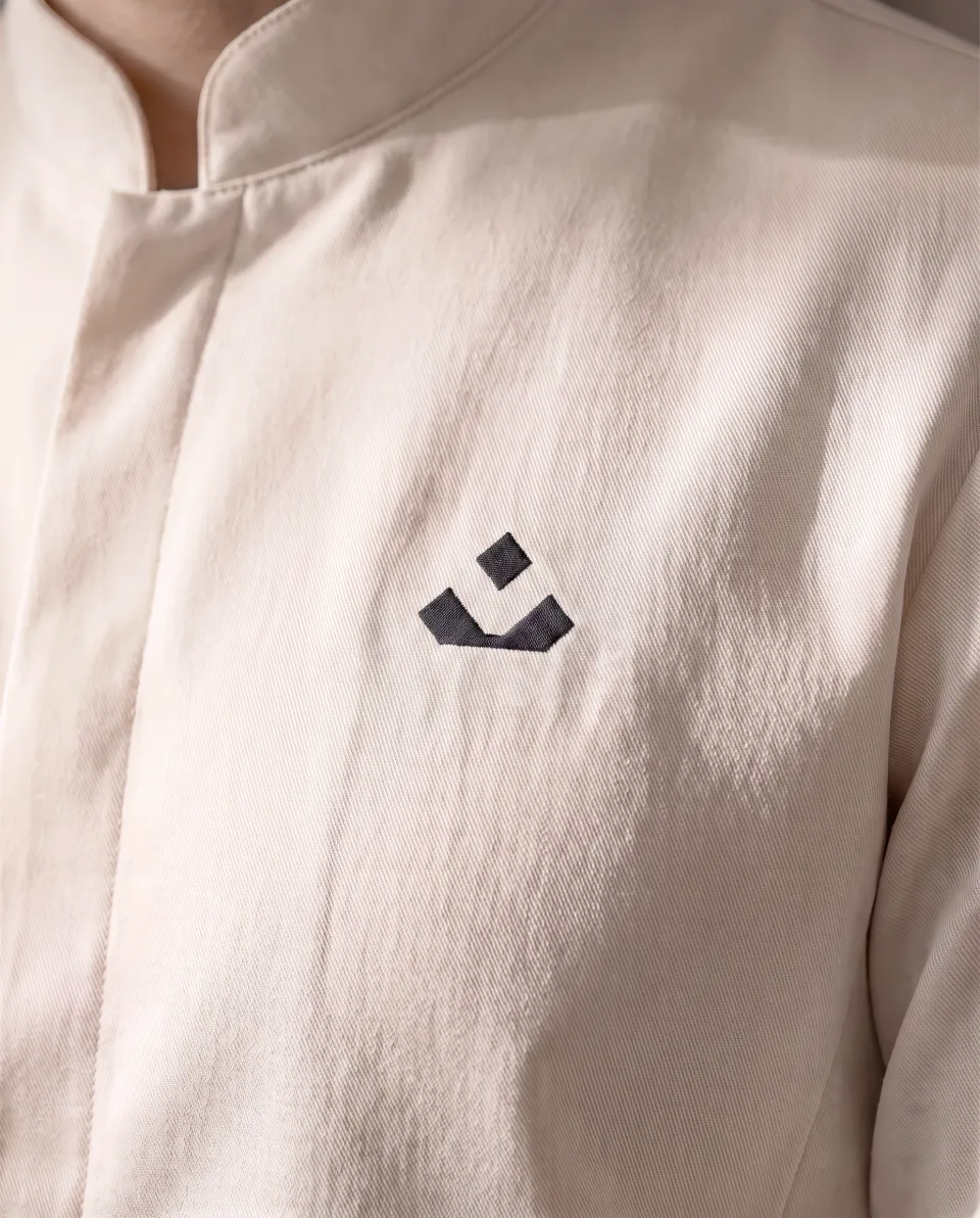 A chef's cream coat with the ATRE hearth mark at the chest