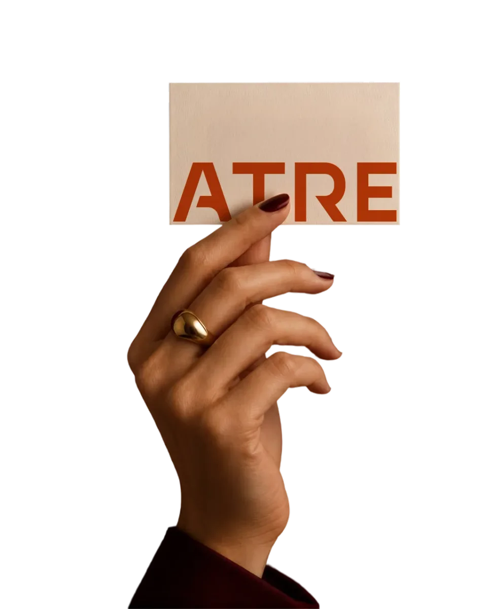A hand holding a cream card with ATRE printed large in orange, against black