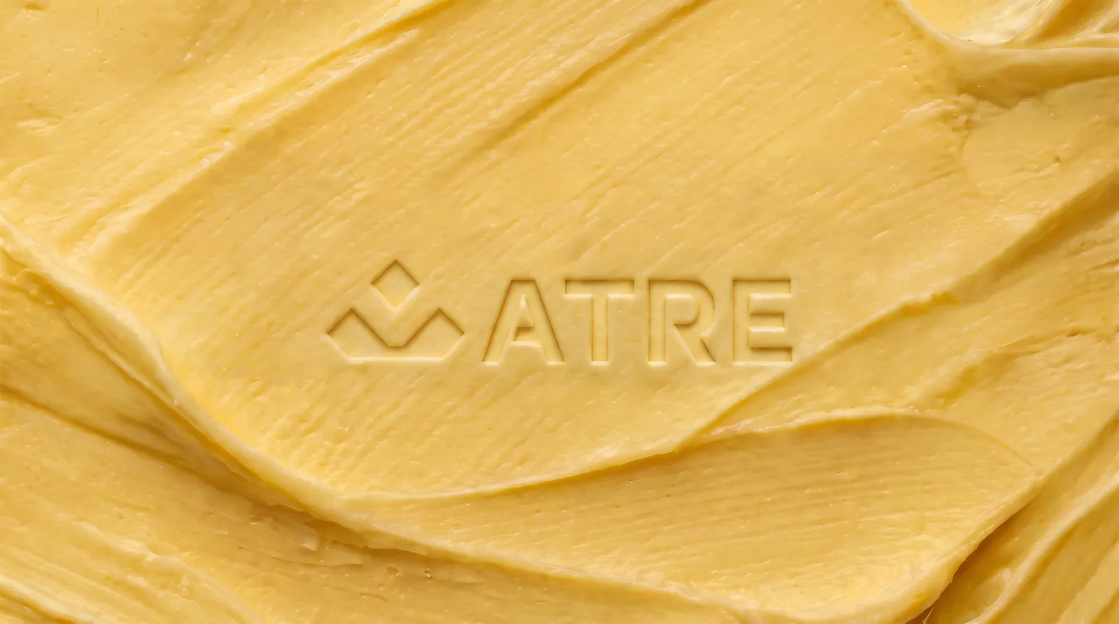 The ATRE mark and wordmark embossed into a swept field of butter
