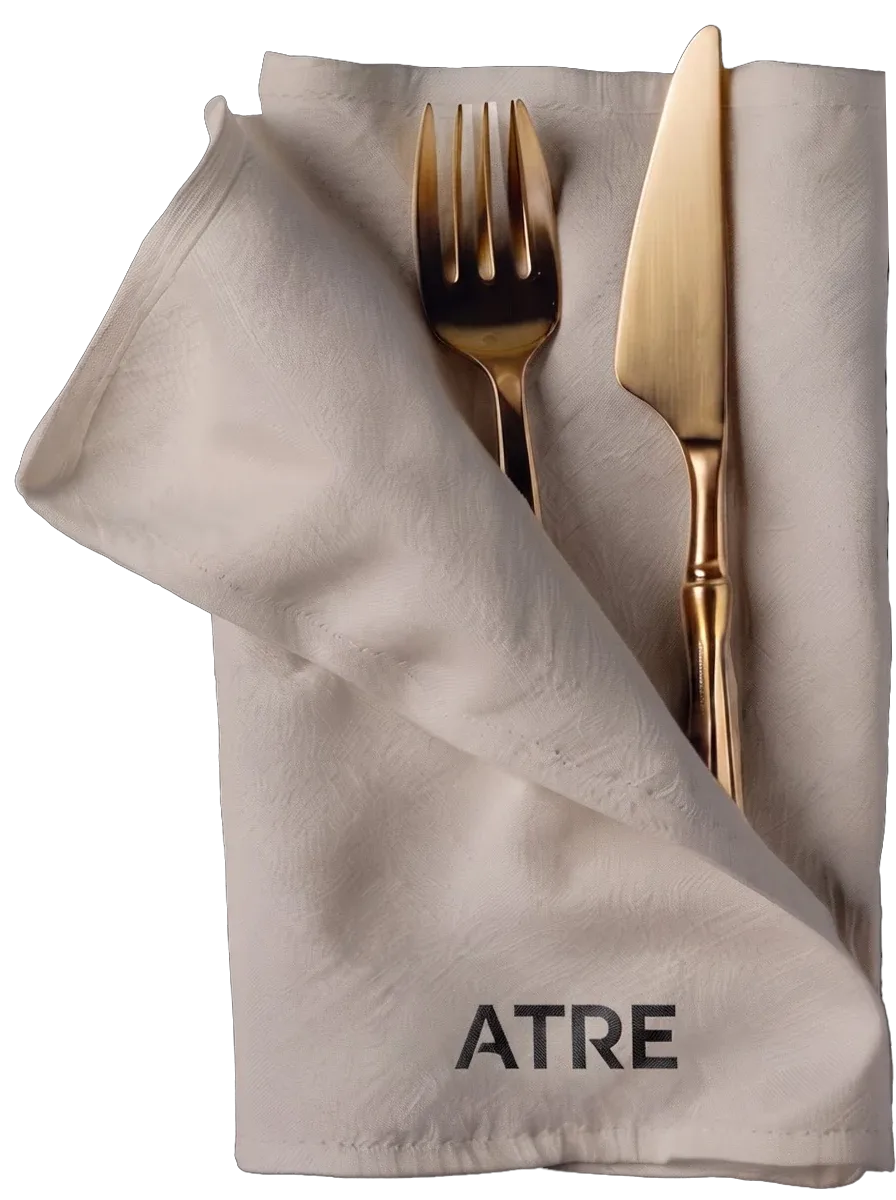 Gold cutlery folded into a cream napkin printed ATRE, on black