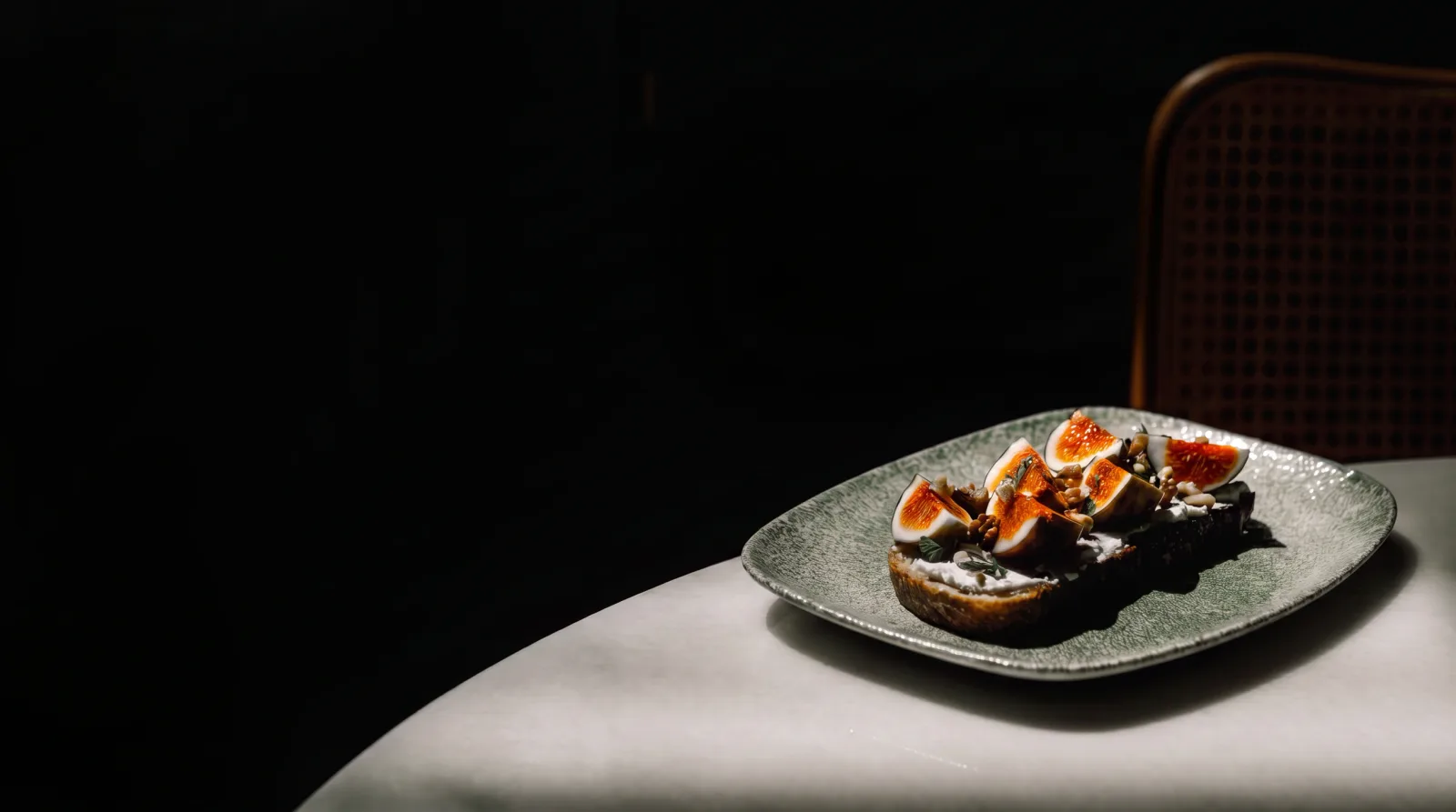 Figs and cheese on toast on a green ceramic plate, on a white table in a dark dining room