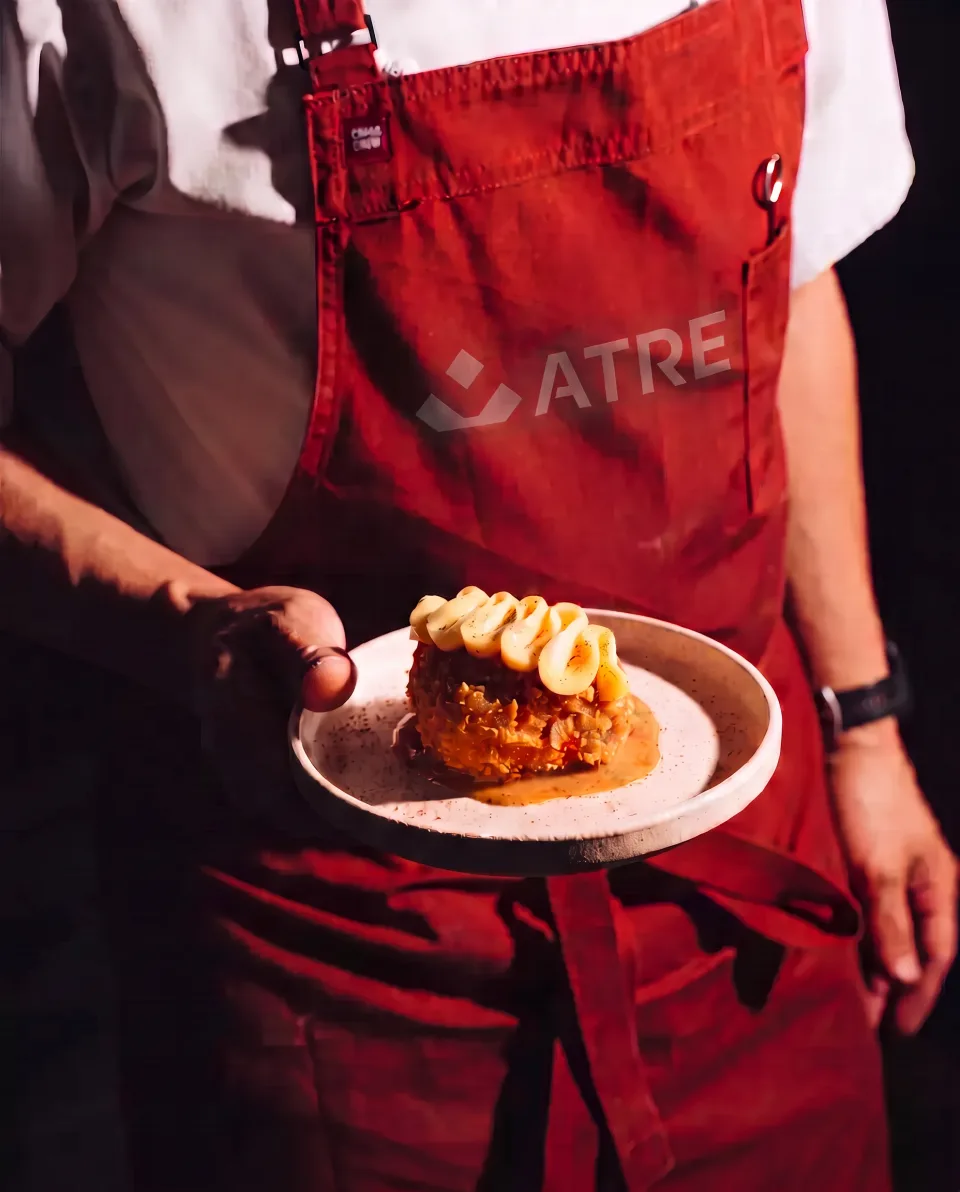 A cook in a red ATRE apron holding a plated dish