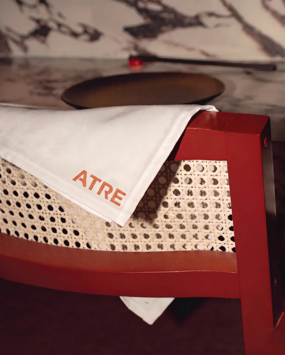 An ATRE napkin folded over the cane seat of a red chair beside a marble counter