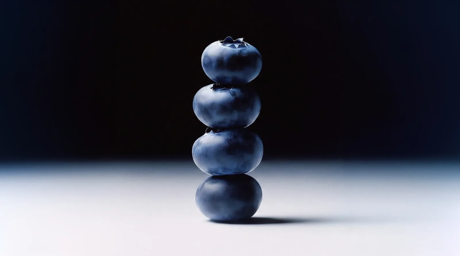 Four blueberries stacked in a column, lit against a graded dark blue ground