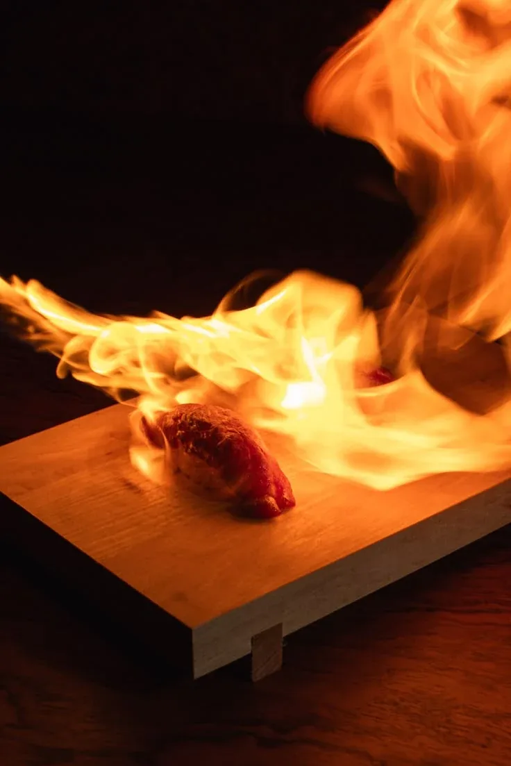 Meat flaming on a wooden board in the dark