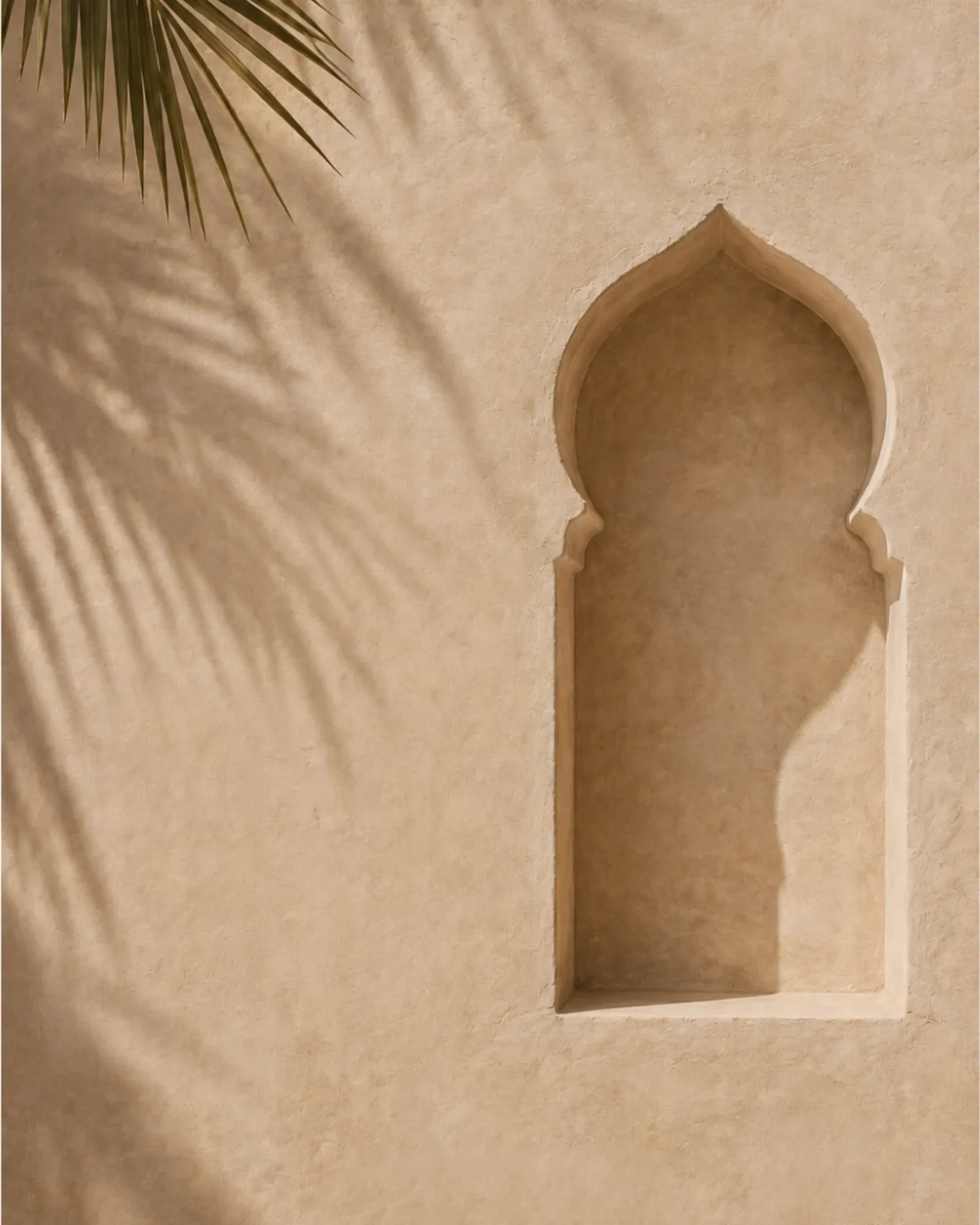 A pointed Omani arch cut into a smooth adobe wall, palm shadows falling across it in the afternoon.