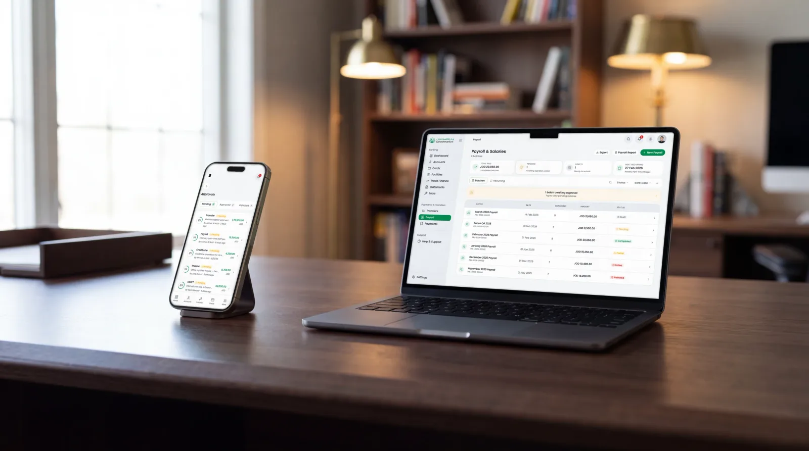 Photograph of a MacBook and an iPhone on a walnut desk, the payroll batches on the laptop and the pending approvals list on the phone: one payroll, the approvers on the phone.
