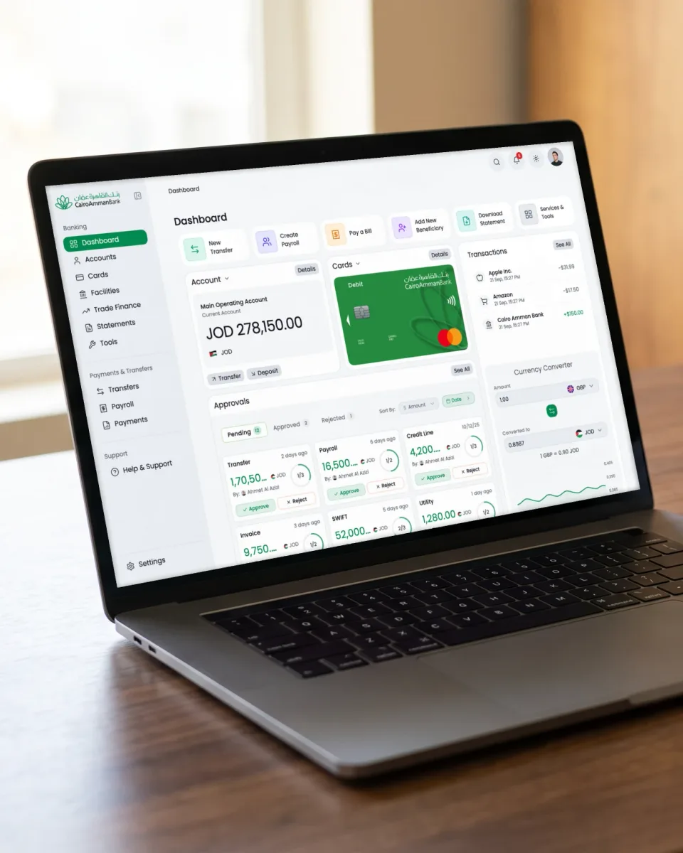 The Cairo Amman Bank corporate banking dashboard on a laptop, on a walnut desk.