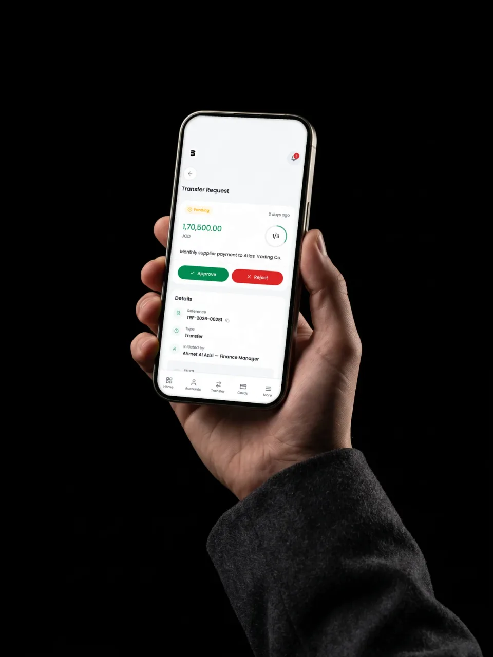 Photograph of a hand holding an iPhone 15 Pro straight to camera on black, a transfer approval on the display with the one-of-three signature ring and the Approve and Reject actions.