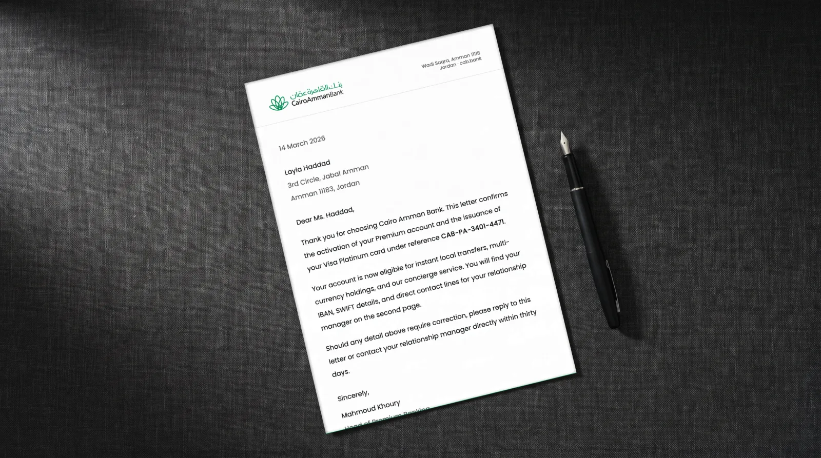 Photograph of the Cairo Amman Bank letterhead on a dark linen desk mat with a fountain pen and a blank business card, the letter itself the real document.
