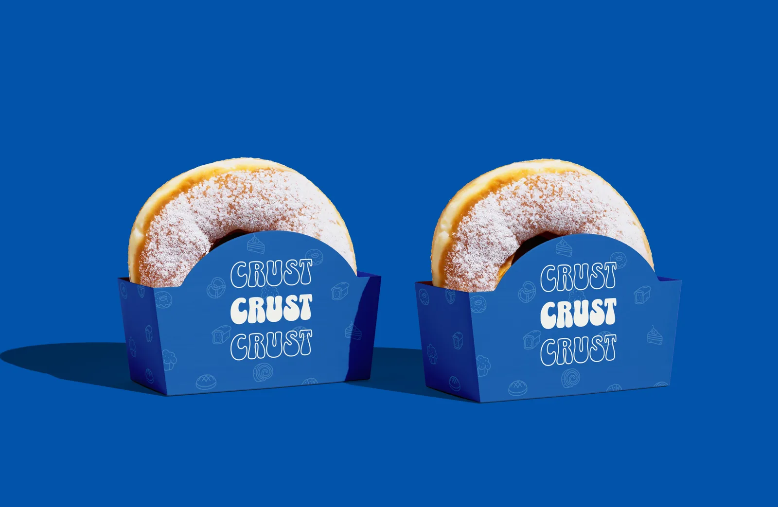 Two sugared doughnuts in blue CRUST branded holders on a bright blue field with chocolate dripping from above