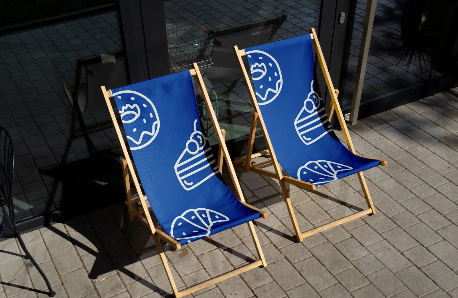 Two blue CRUST branded deck chairs printed with white bakery icons on a sunlit terrace