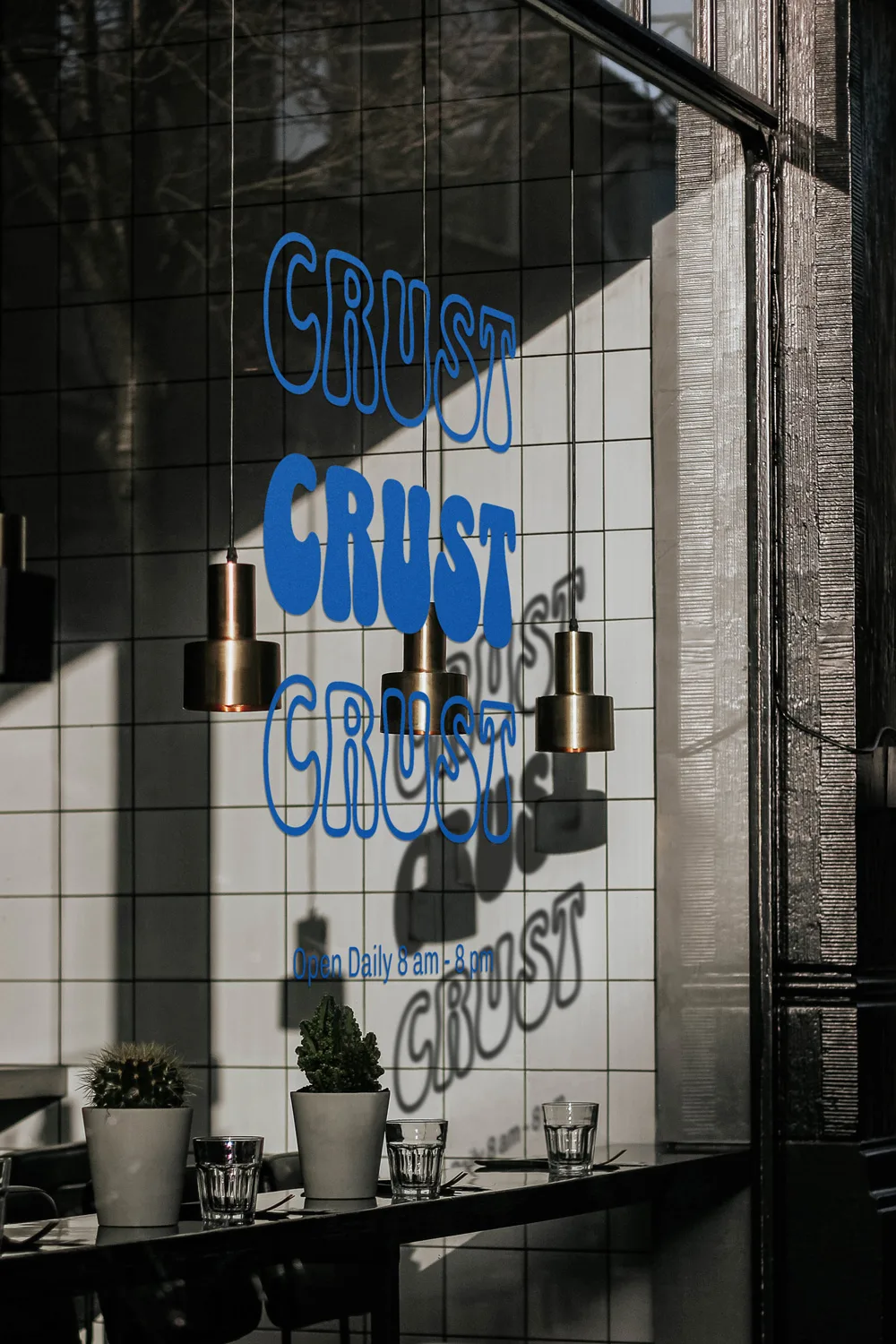 CRUST window graphics: the wordmark repeated down a sunlit storefront window above potted plants and brass pendant lamps