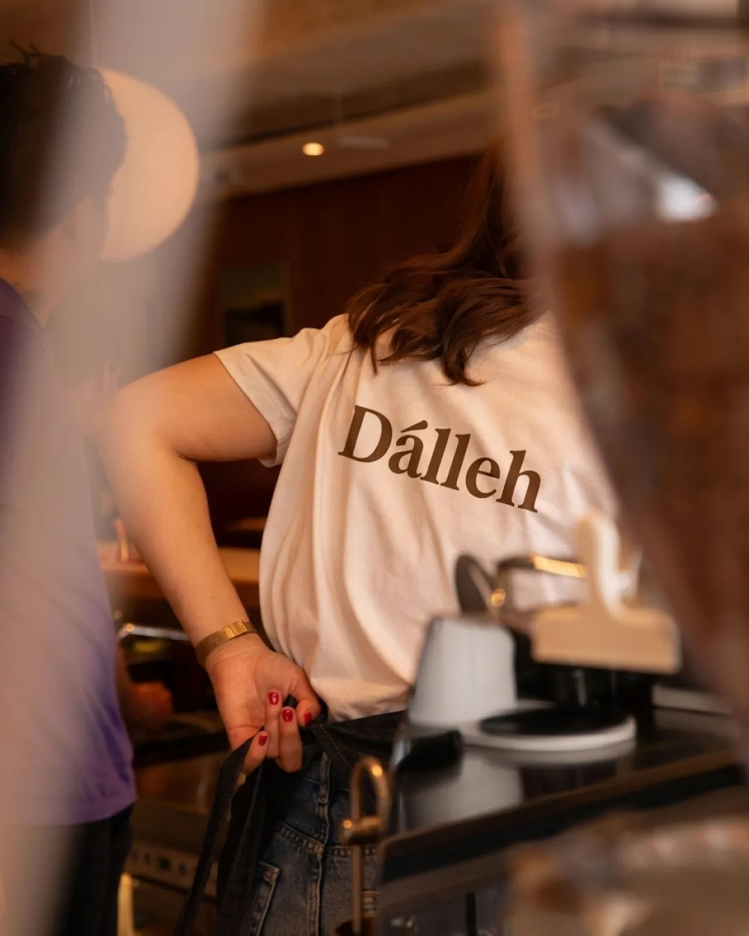 Barista at the espresso machine wearing the cream Dalleh tee with the brown logotype
