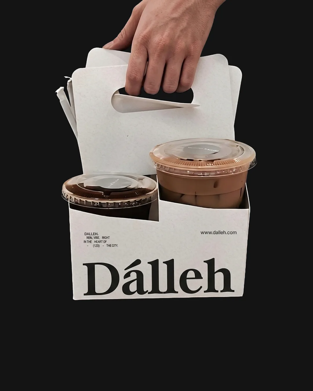 Hand lifting a cream Dalleh cup carrier with two iced coffees against a near black ground