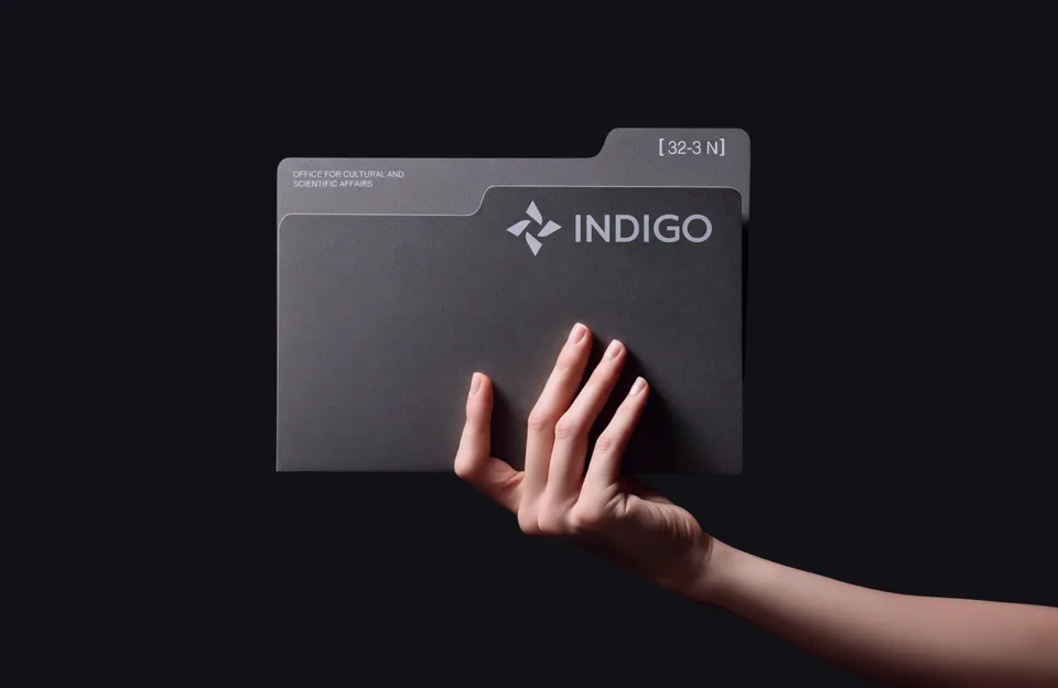 Hand holding a grey tabbed Indigo document folder marked with an office designation and the index 32-3 N