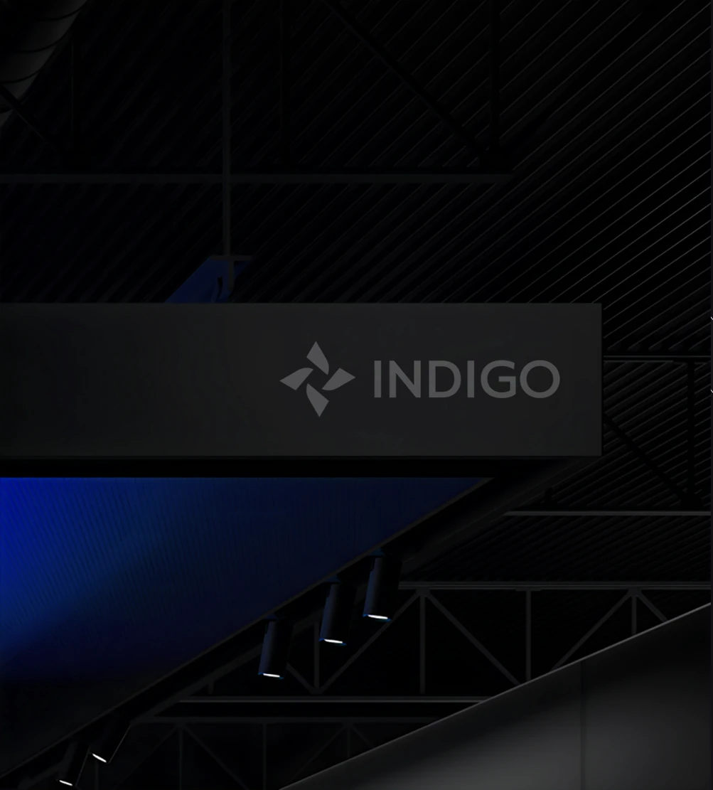 Indigo signage in a dark exhibition hall, the lockup lit on a suspended fascia