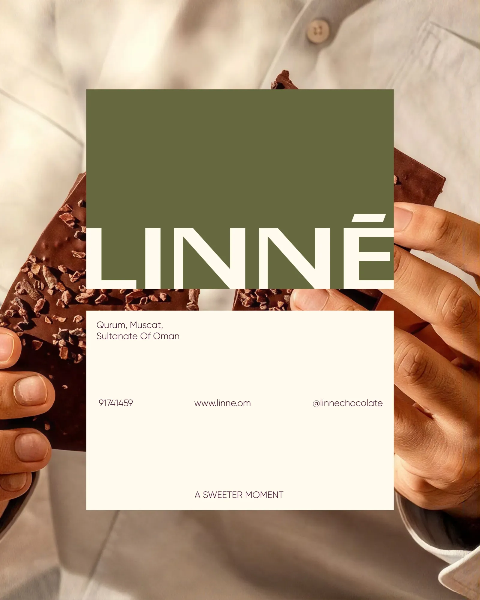 The LINNÉ business card held over a slab of chocolate broken in two hands: the Latin wordmark on olive above, and on cream the Qurum, Muscat address, the website and the Instagram handle.