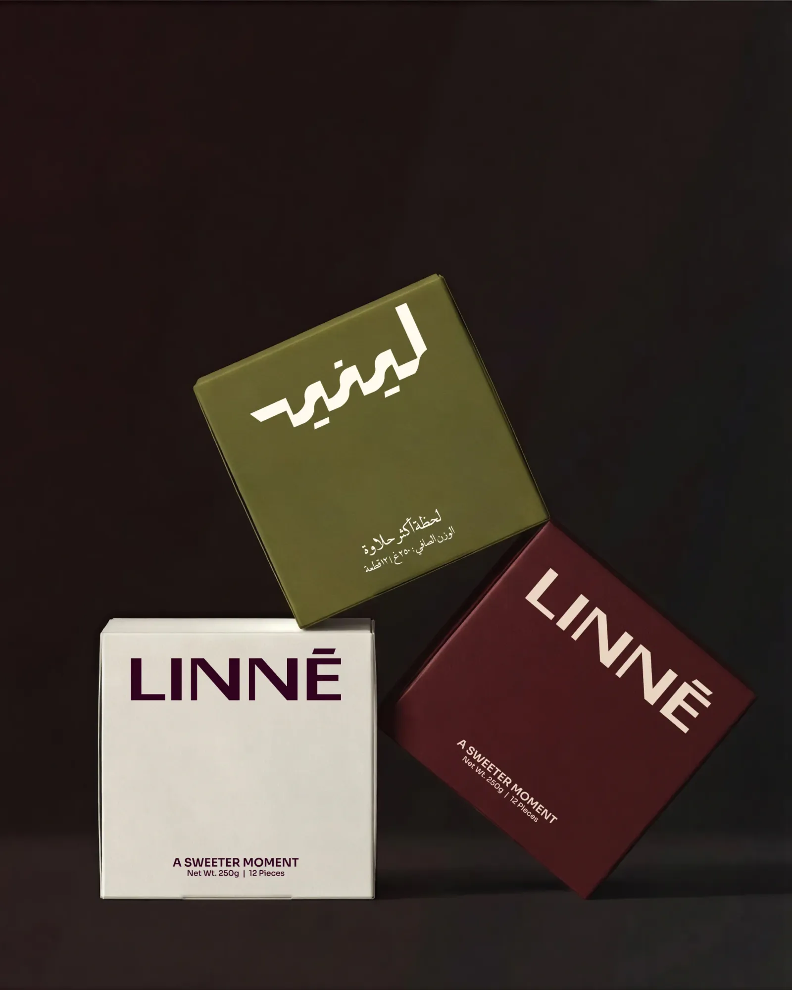 Three LINNÉ gift boxes stacked on a dark ground: olive with the Arabic wordmark, cream with the Latin wordmark, and maroon reading A Sweeter Moment, 250 grams, 12 pieces.