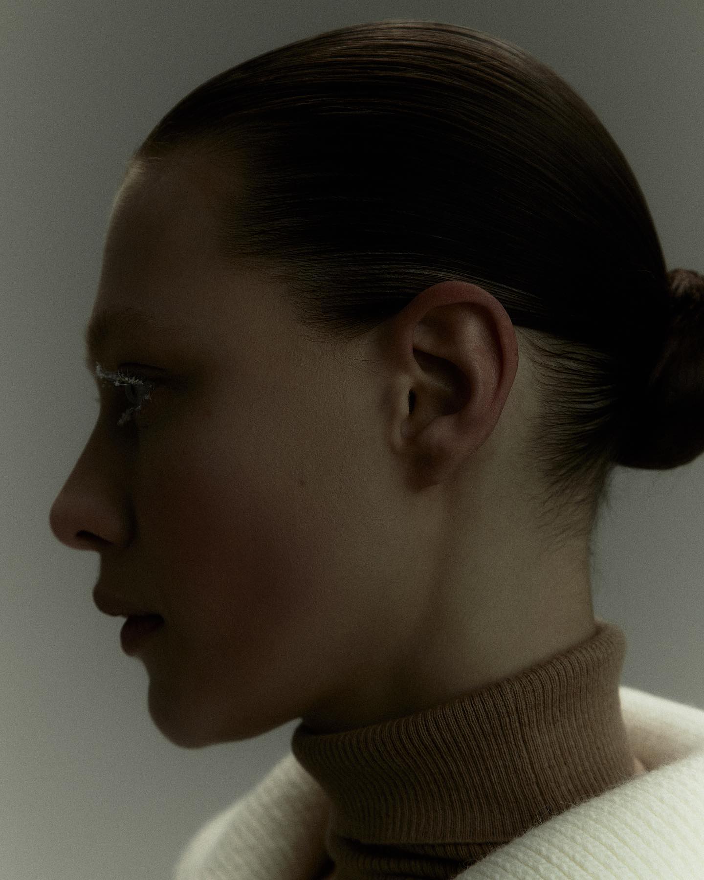 Profile portrait of a model with hair drawn back, in a cream turtleneck