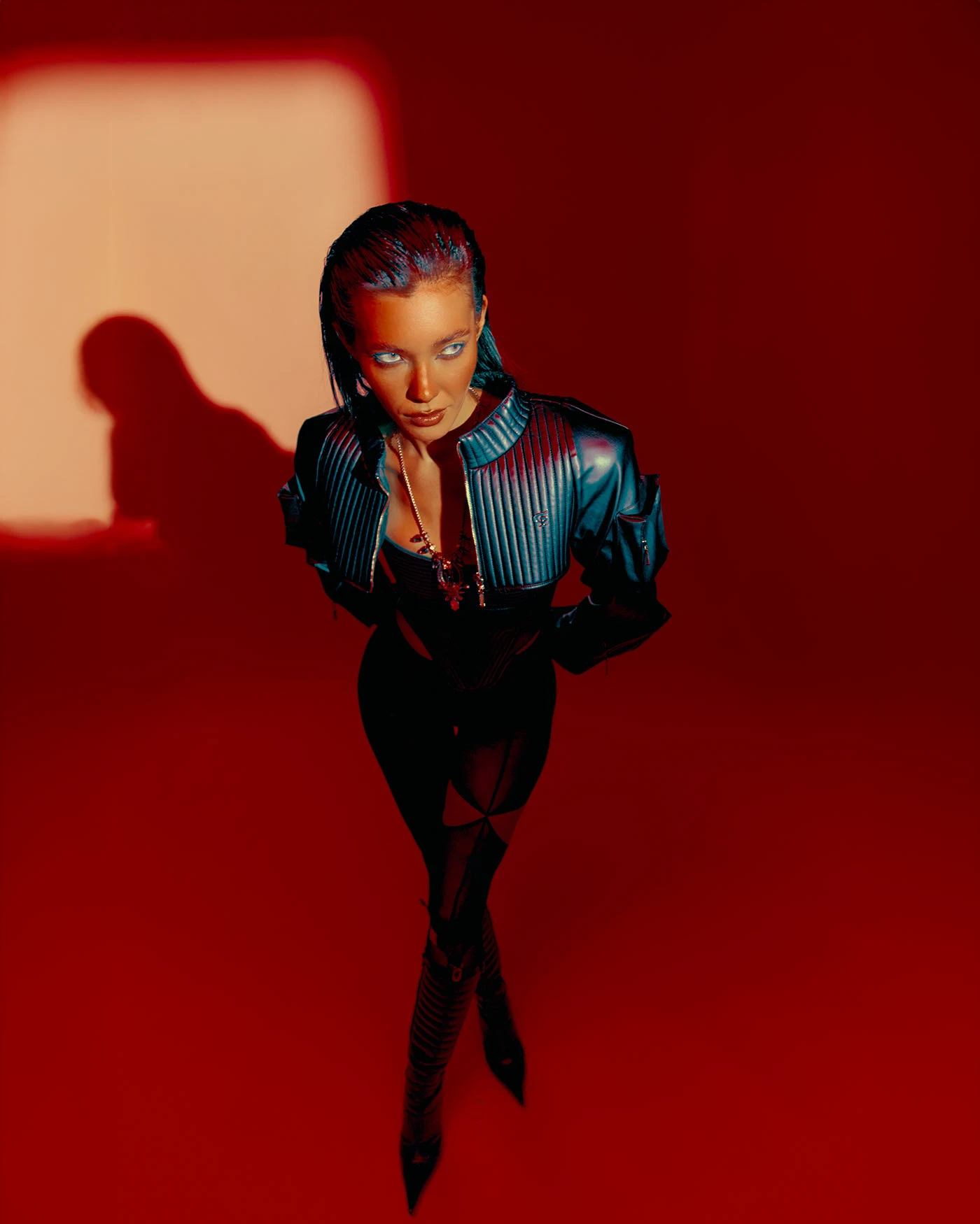 Red gel campaign frame shot from above: a model standing in a long shadow, seen from overhead
