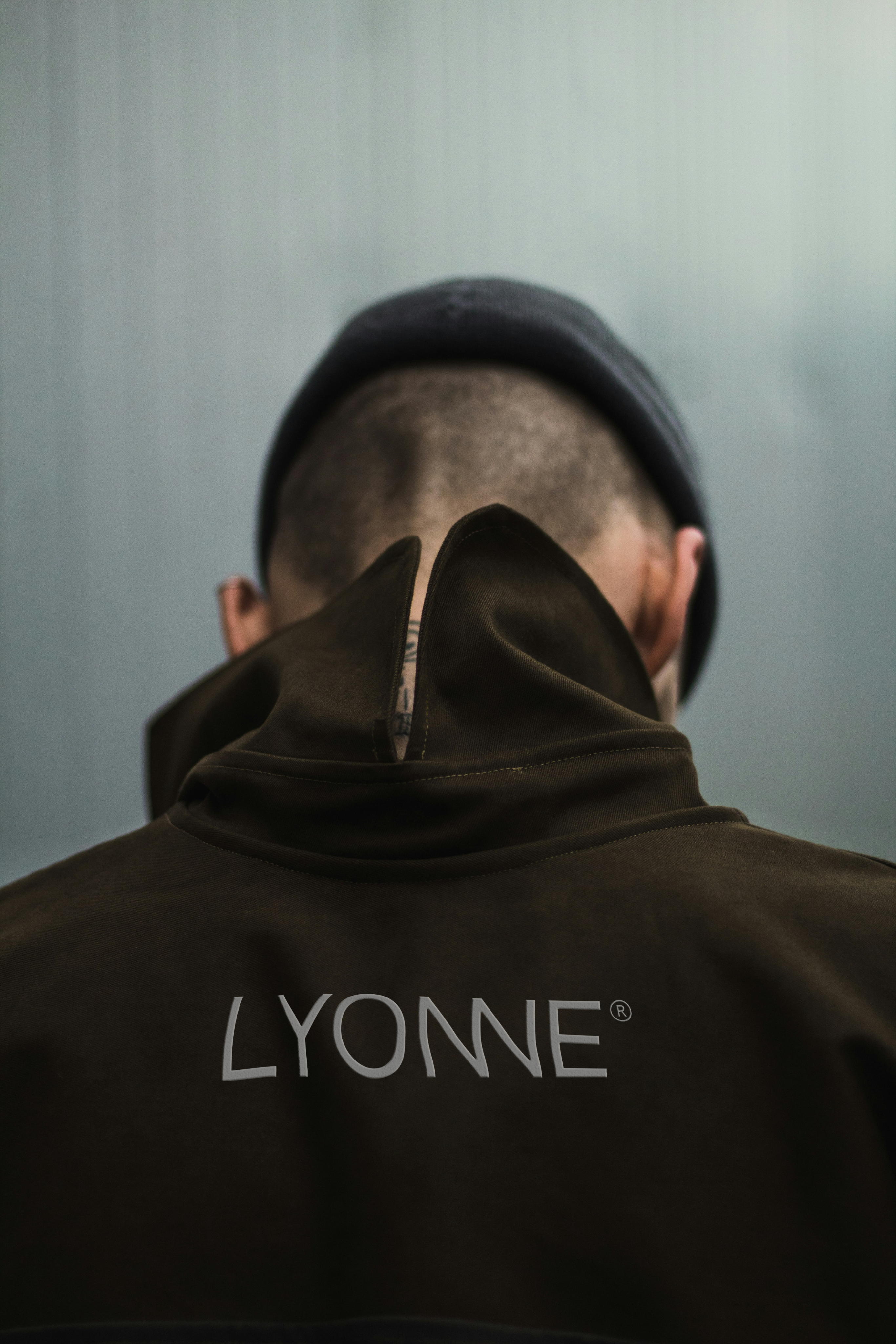 Back of a dark Lyonne hoodie with the tonal wordmark print, hood up