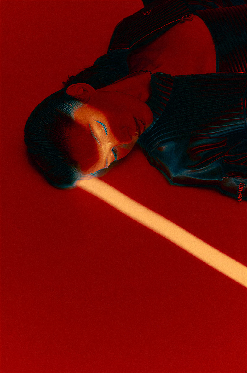 Red gel campaign frame: a model lying back with a hard bar of warm light across the frame