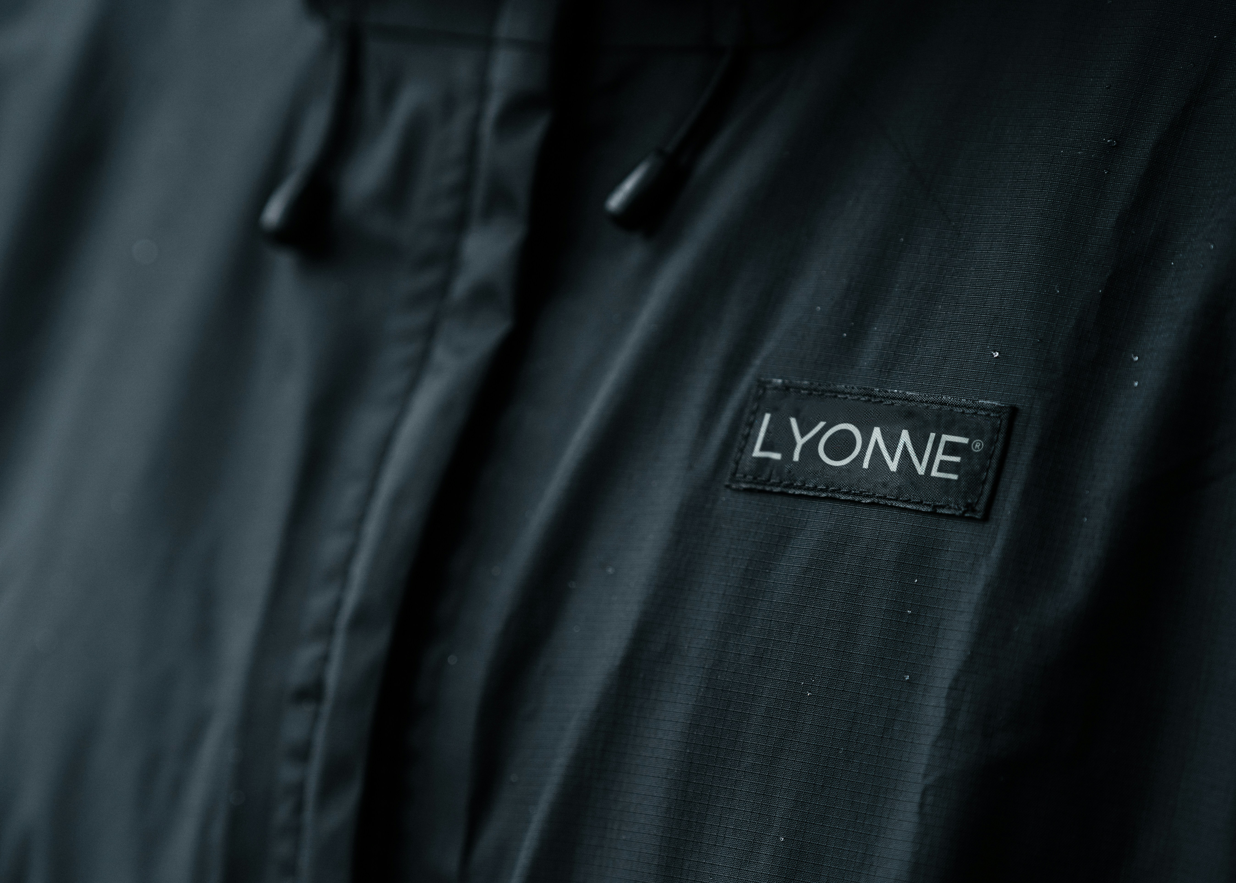 Close detail of the woven Lyonne label stitched to a dark green technical jacket