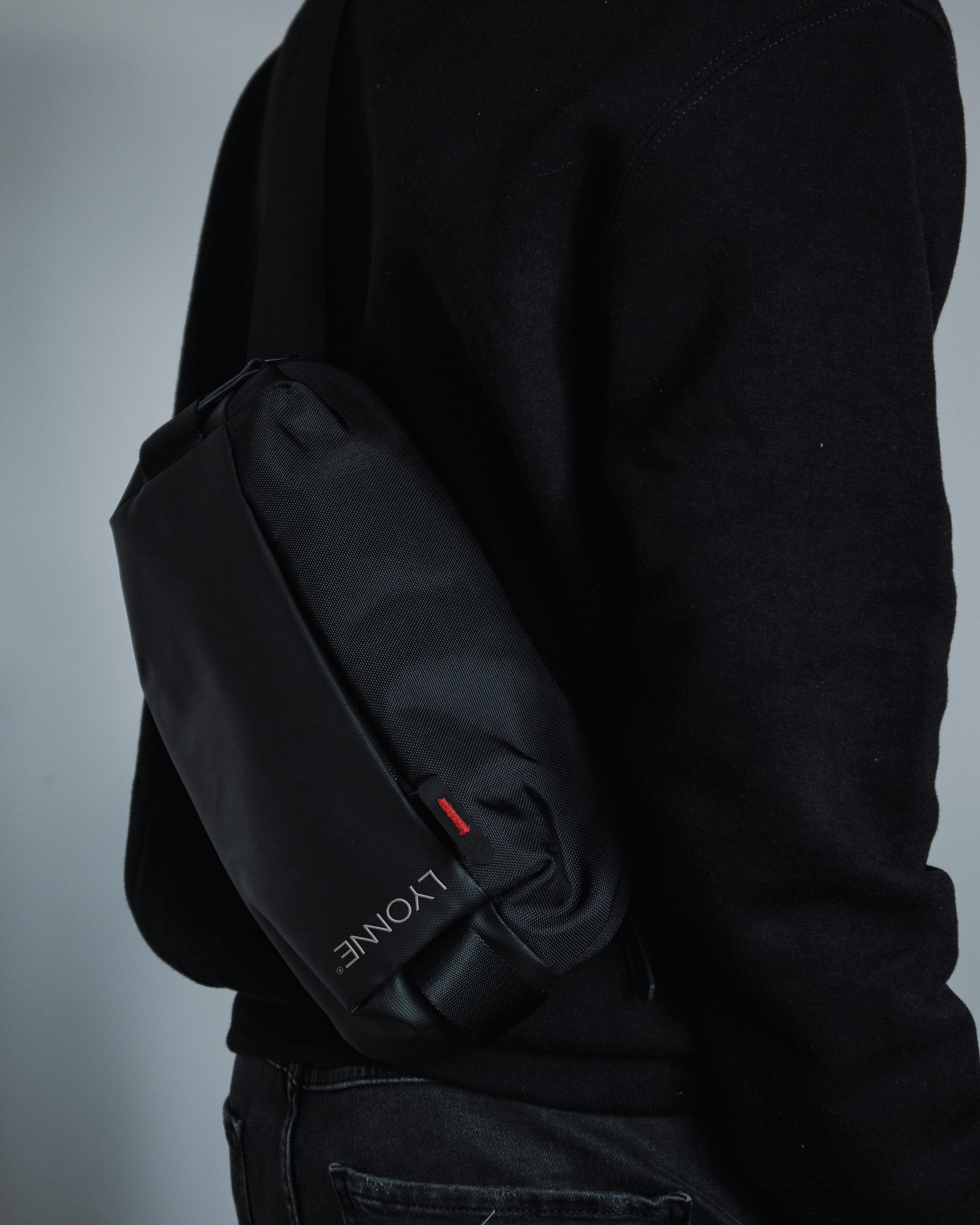 Black crossbody bag with a red woven Lyonne tab, worn across a black sweatshirt