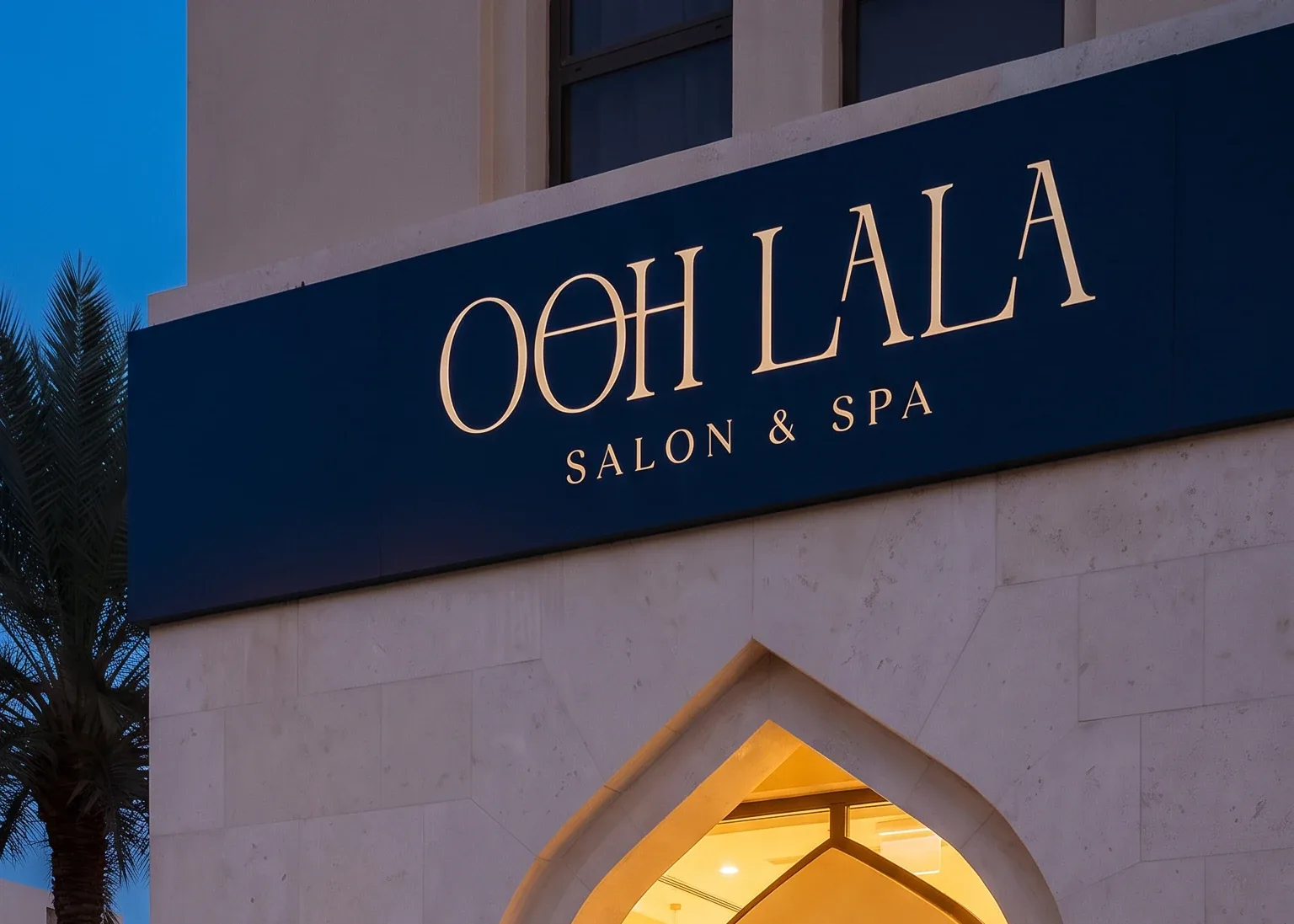 The Ooh Lala fascia in navy at dusk, the wordmark and SALON & SPA in warm metal, above the pointed arch doorway lit from within