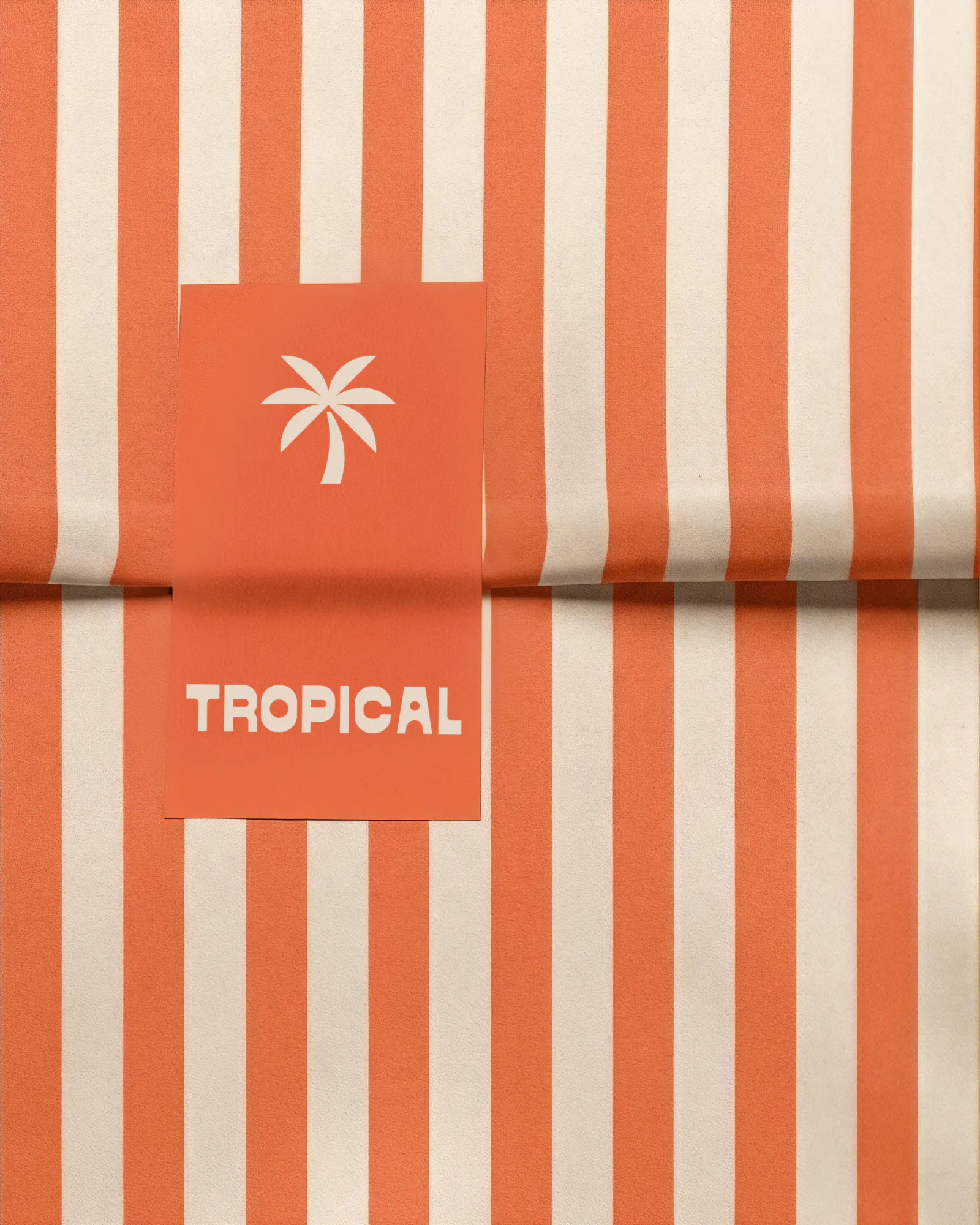 A coral and cream striped paper bag sealed with a coral label carrying the palm and the Latin wordmark.