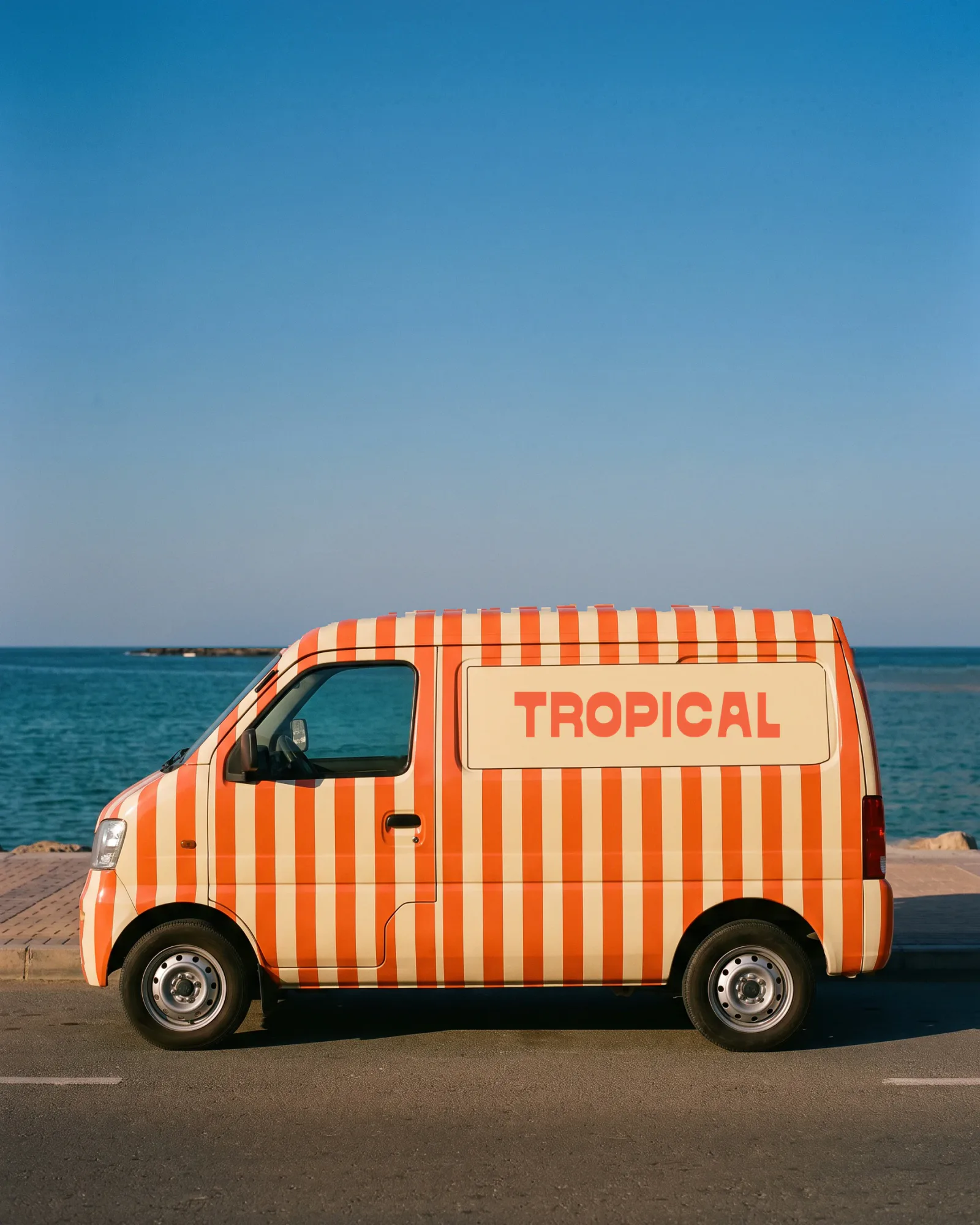 A generated concept image: a delivery van wrapped in coral and cream stripes with the Latin wordmark, by the sea.