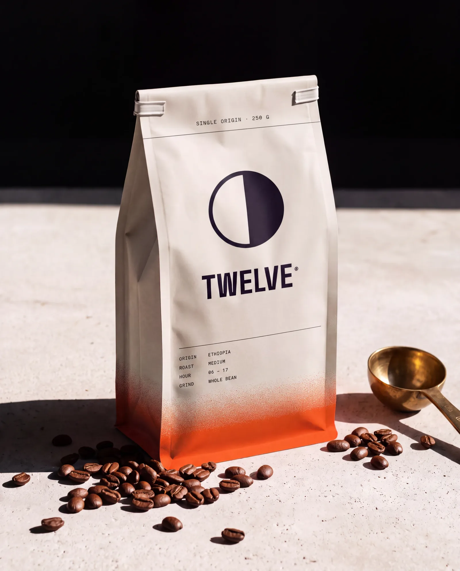 A bone TWELVE coffee bag standing on a concrete counter beside spilled beans and a brass scoop, in hard morning sun