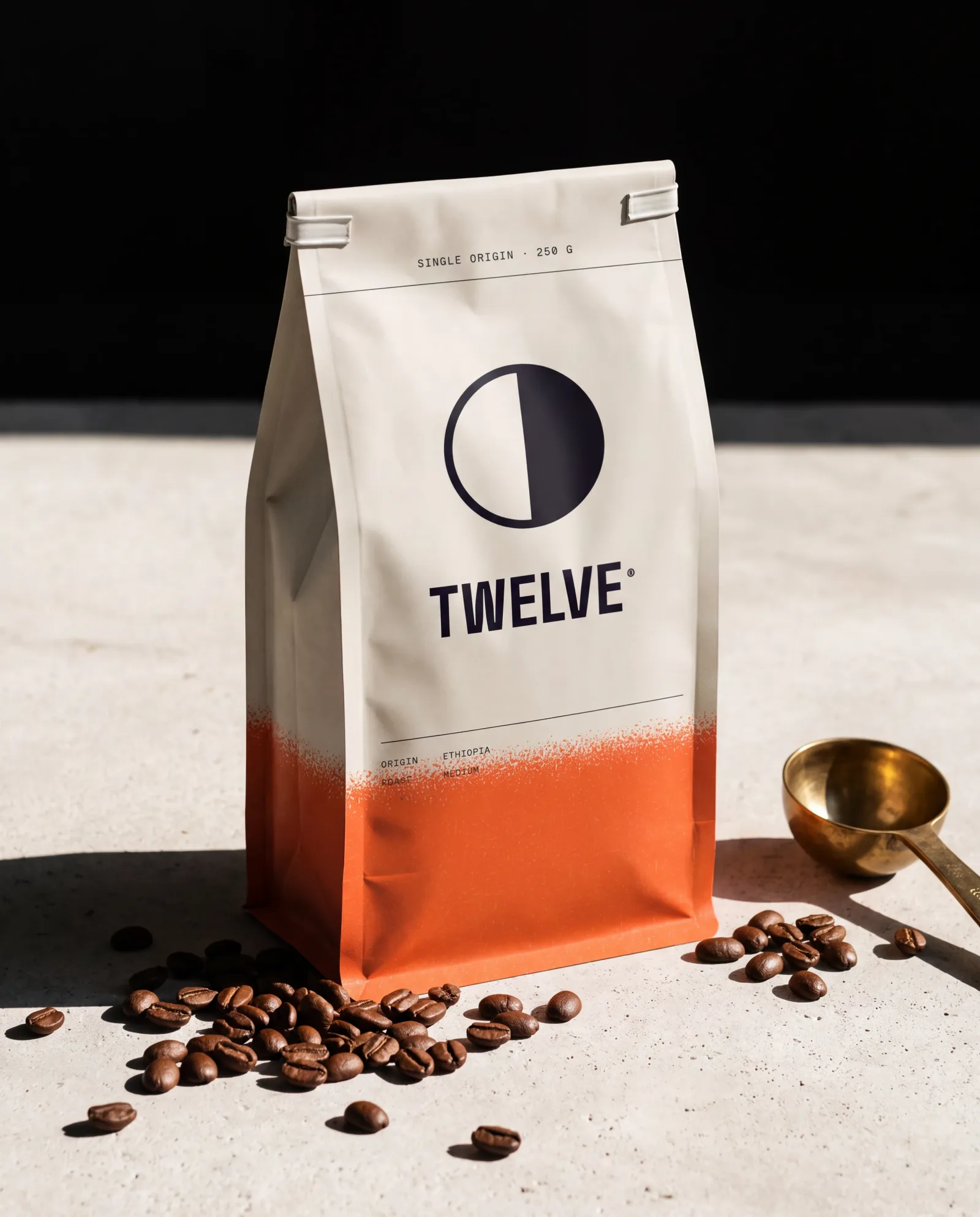 A bone TWELVE coffee bag standing on a concrete counter beside spilled beans and a brass scoop, in hard morning sun