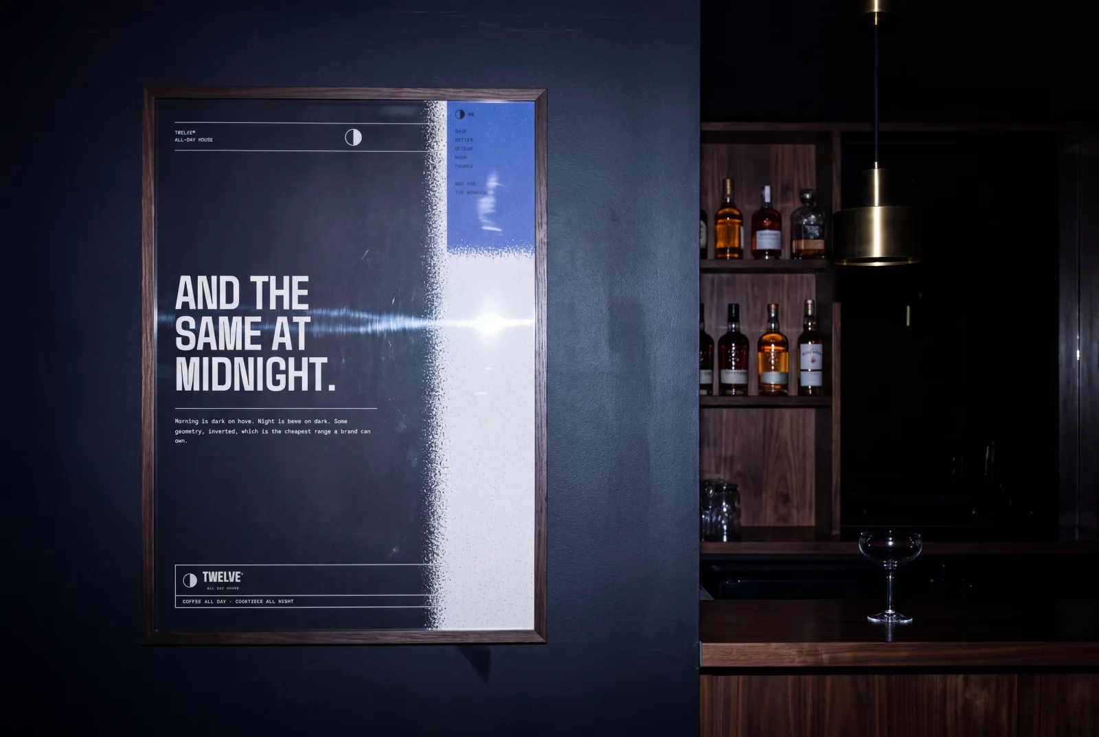 The TWELVE night poster framed on a dark bar wall, caught by a direct flash with the backbar falling into black