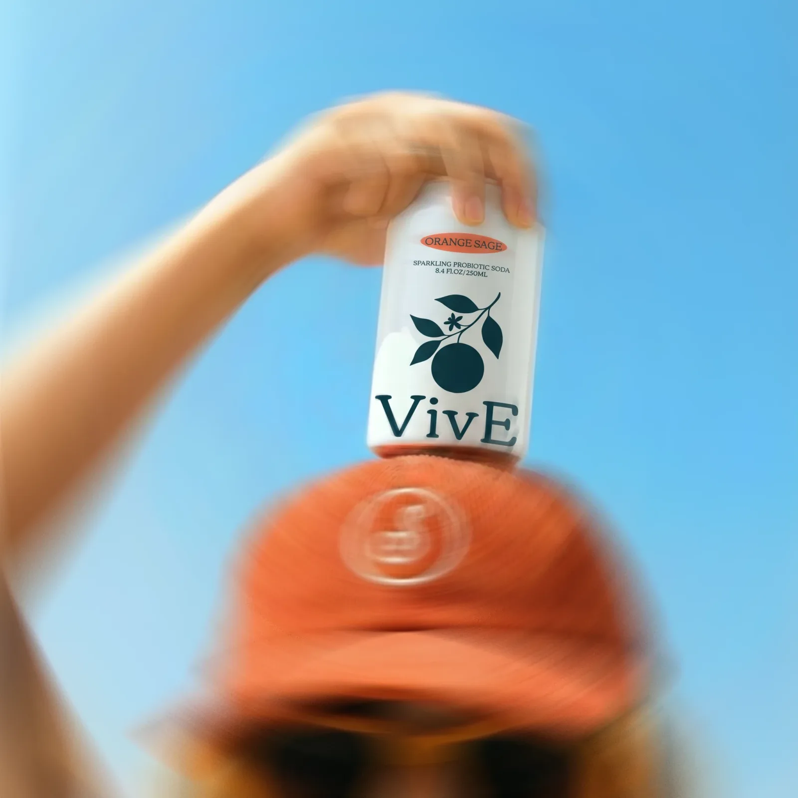 A VivE can held up over a red cap against blue sky, the whole frame streaked with motion blur