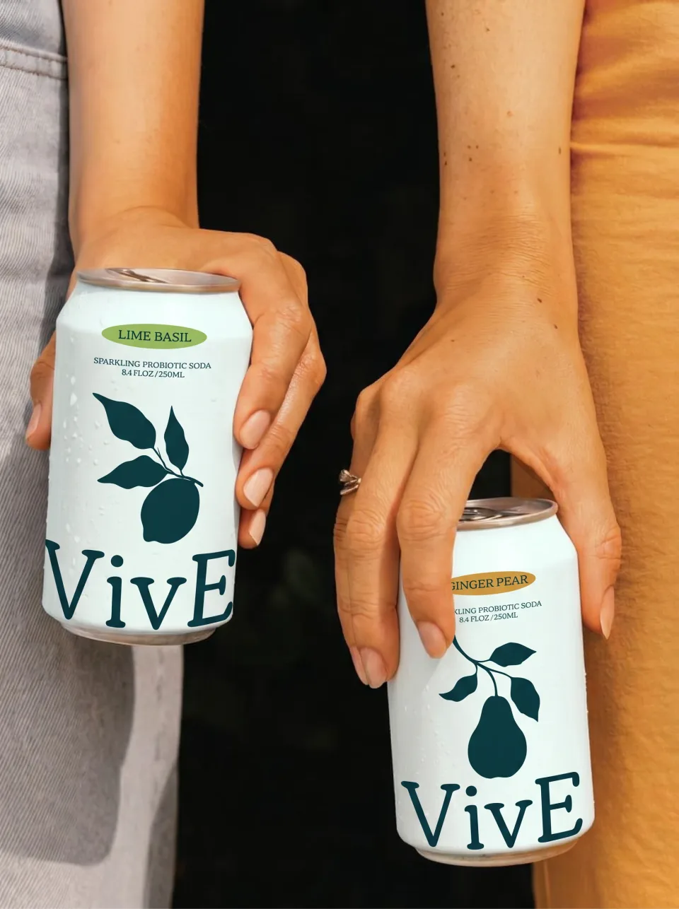 Two hands holding a Lime Basil and a Ginger Pear can against orange and denim